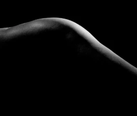 Curve in Rim Light Black and white bodyscape detail of a male model’s hip and glute curve, defined by rim light against a dark background.
