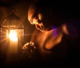 Figure by Lantern Light Candlelit fine art image of Larry seated beside a lantern, with warm light illuminating his face and upper body against a dark background.