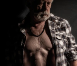 Portrait in Plaid and Shadow Dramatic color portrait of Larry wearing an open plaid shirt, looking downward in strong side lighting against a dark background.