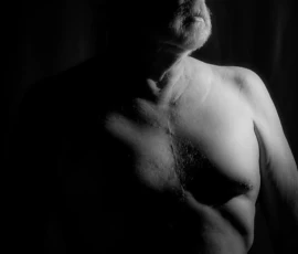 Portrait in Light and Shadow Black and white portrait of Larry with bare torso, looking upward in dramatic side lighting against a dark background.