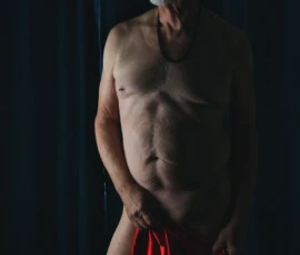 Upward Gaze with Red Drape
Photo by Rebel Jones Fine art figure study of Larry standing with a red drape, looking upward in dramatic low-key lighting against a dark background.